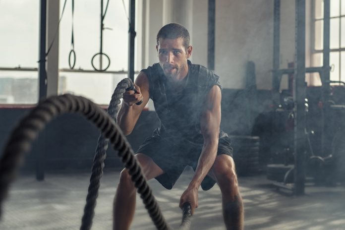 Seorang laki-laki tengah fokus berolahraga battle ropes (Sumber: Envato)