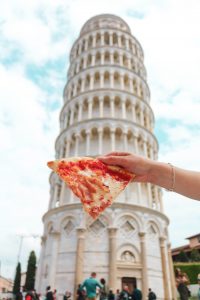Sepotong makanan pizza di depan Menara Pisa, Italia (Photo by Anna Church on Unsplash)