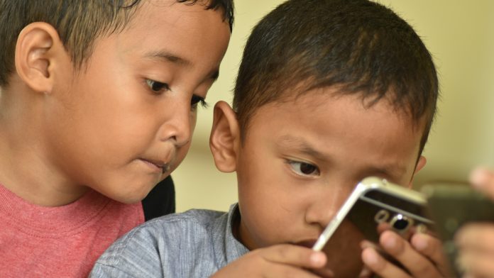 Ilustrasi dua anak laki-laki sedang membaca konten buku dalam smartphone (Source: unsplash.com; Taken by: Budi Gustaman)